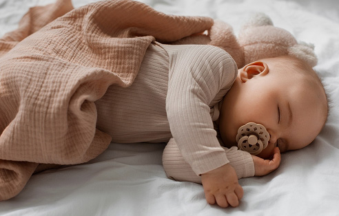 Slapende baby met speen op een lichtroze deken.